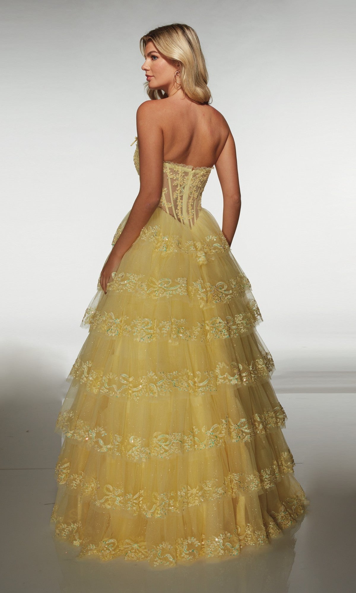A woman stands facing away on a plain background, wearing the Alyce 62191 long prom dress, which features a strapless bodice, tulle A-line skirt, and floral embroidery.